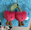 Plush cherry keychain held against a blue background with cartoon characters.