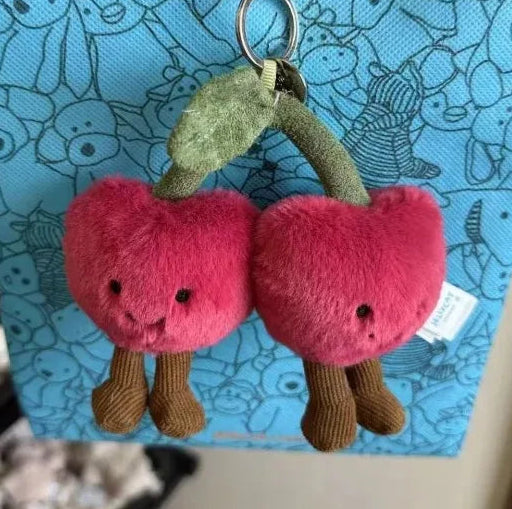 Plush cherry keychain held against a blue background with cartoon characters.
